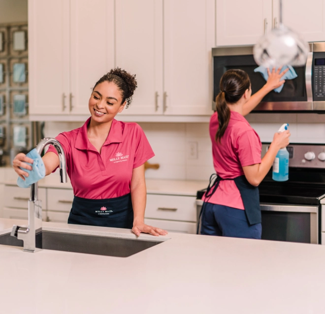 Molly Maid professionals wiping the counter and microwave in a white kitchen